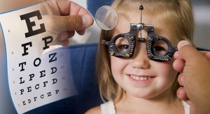 Optometrist In Exam Room With Young Girl In Chair Smiling